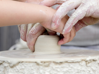 Artisan learning a child to make potter from white clay.