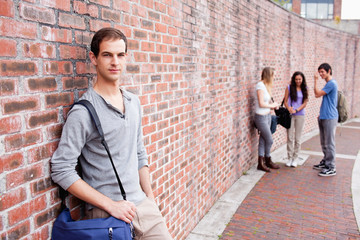 Fototapeta na wymiar Student leaning on a wall while his friends are talking