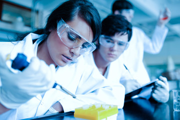 Young scientist dropping liquid in test tubes while her partner