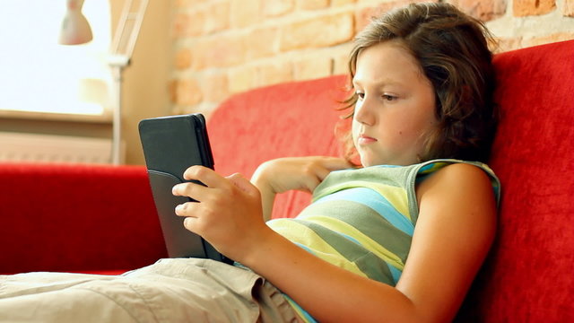Young teenager with ebook reader on sofa, steadicam shot