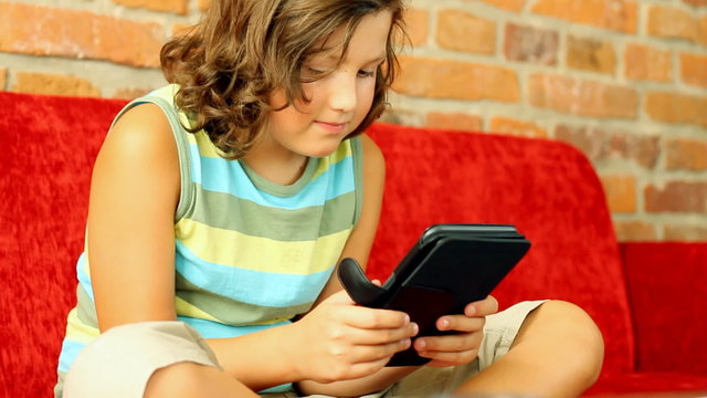 Young teenager with ebook reader on sofa, steadicam shot