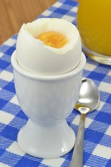 A boiled egg in a cup on the breakfast table with orange juice