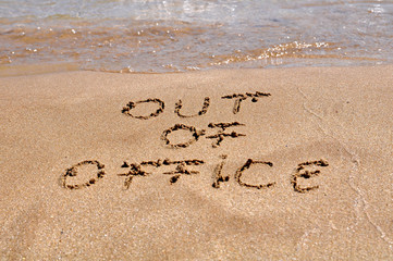 Out of office text written on the beach sand