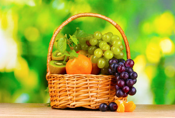 Ripe juicy fruits in basket on wooden table on green background