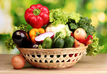 Fresh vegetables in basket on  wooden table on green background