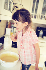 Little child girl tasting batter in kitchen