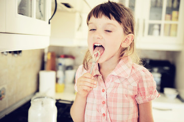 Little child girl tasting batter in kitchen