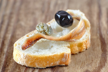 Slice of bread with anchovy fillet, caper and olive