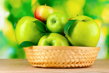 Fresh organic green apples in basket on wooden table outside