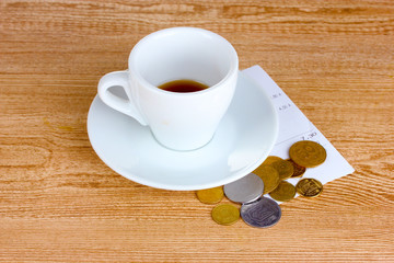 Empty cup of coffee with coins tip on wooden background
