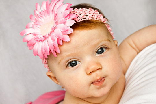 Baby girl with bright eyes posing with pink flower band