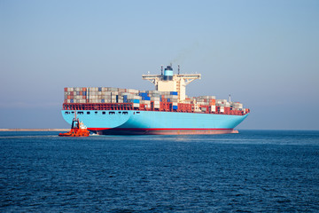 Container ship leaves the port, assist by a tugboat.