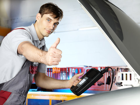 Young motor mechanic is tuning the engine of a car