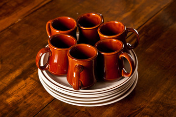 Six brown coffee mugs sitting on top of a stack of plates