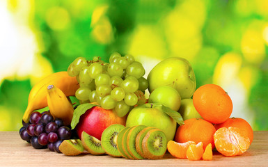 Fototapeta na wymiar Ripe juicy fruits on wooden table on green background
