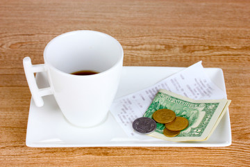 Empty cup of coffee with five dollars tip on wooden background