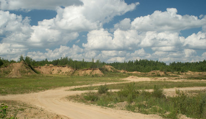 Rural landscape with sandy hills and forest under cloudy sky