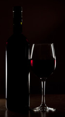 Backlit detail of a glass of red wine and the  bottle