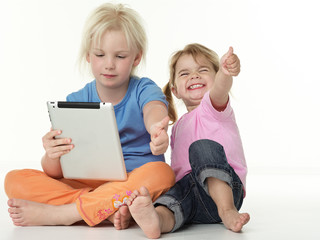 Adorable little girls seated on the floor playing with touchpad