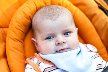 Little baby boy with blue eyes in orange stroller