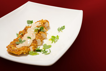 Pan fried pine nut chicken breast on plate against red
