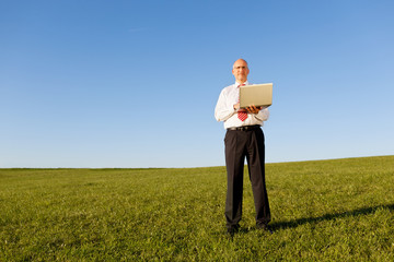 mann mit laptop steht auf einer wiese