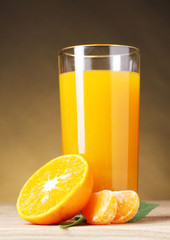 Tangerines and juice glass on wooden table on brown background
