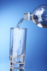 Pouring water on glass on blue background