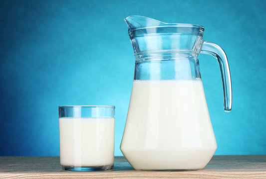 Tasty milk in jug and glass on blue background