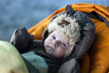 Little baby boy in orange stroller in winter clothes