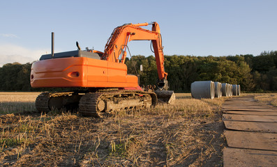 An orange excavator and huge sewer pipes on a field