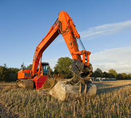 An orange excavator and huge sewer pipes on a field