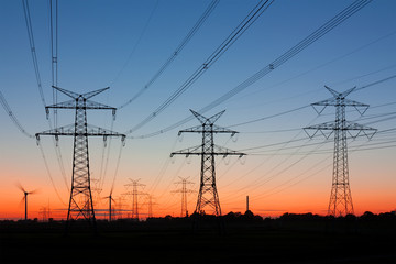 Strommasten bei Sonnenuntergang, am Horizont Windräder