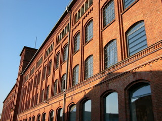 Fensterfront einer alten Fabrik mit Fassade aus Backstein vor blauem Himmel im Sonnenschein in der...