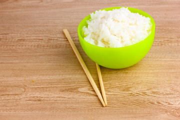 Green bowl of cooked rice and chopsticks on wooden table