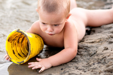 Little boy playing in the sand with plastic can