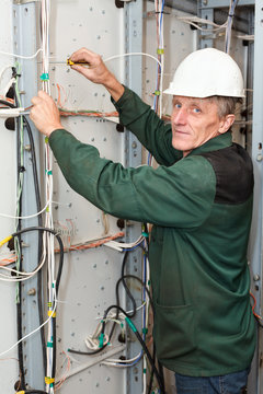 Mature electrician working in hard hat with cables and wires