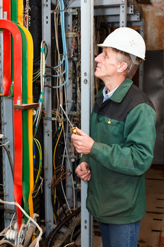 Mature electrician working in hard hat with cables and wires