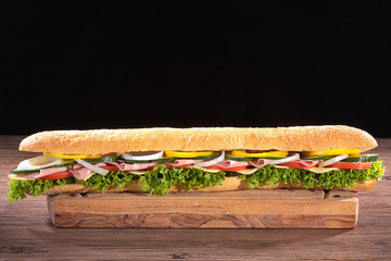 Sandwich baguette rießig mit Wurst, Käse und Salat auf Holzbrett Nahaufnahme