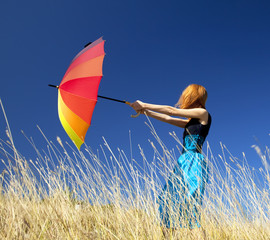 Redhead girl with umbrella at windy grass meadow.
