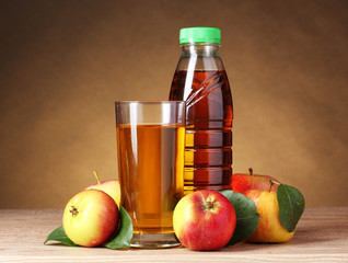 Apple juice and apples on wooden table on brown background