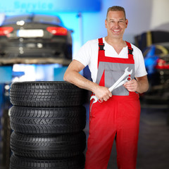 Motor mechanic in a garage next to a set of winter tyres