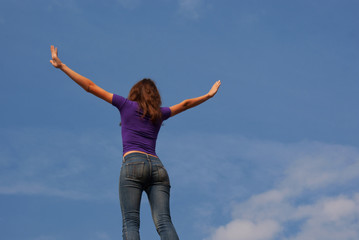 Young woman staying with raised hands against blue sky