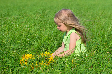 Little girl weaves a wreath of yellow flowers