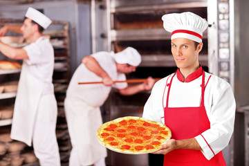 Male baker holding a pizza in bakery