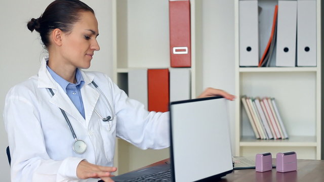 Happy female doctor finishing work on laptop in the office
