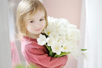 Adorable smiling little girl with tulips by the window