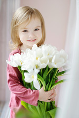 Adorable smiling little girl with tulips by the window