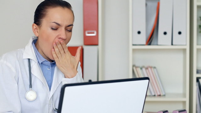 Overworked female doctor sitting at the desk and yawn