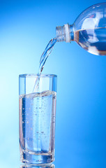 Pouring water on glass on blue background